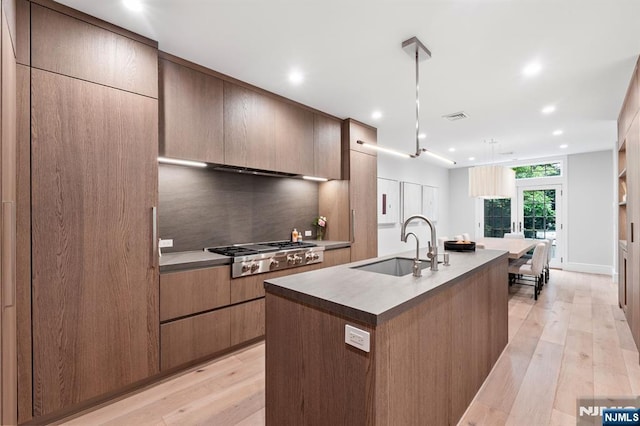10 Kensington Ct, Tenafly, NJ 07670 - kitchen with stainless steel gas stovetop, a sink, light wood-style flooring, decorative backsplash, and a kitchen island with sink