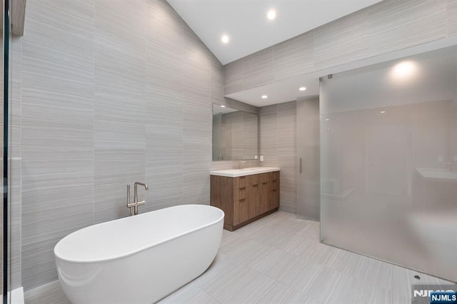 10 Kensington Ct, Tenafly, NJ 07670 - bathroom with tile walls, vanity, a freestanding tub, vaulted ceiling, and a shower with door