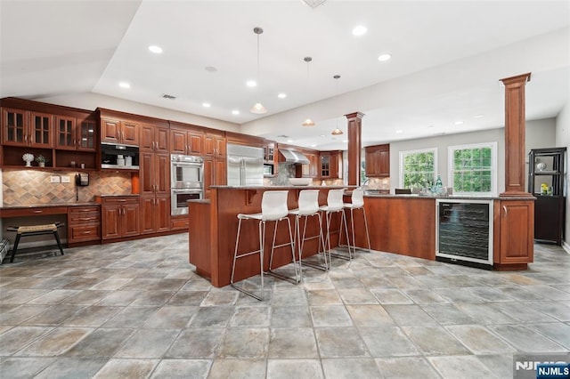 15 Fred St, Old Tappan, NJ 07675 - kitchen featuring beverage cooler, ornate columns, appliances with stainless steel finishes, wall chimney range hood, and tasteful backsplash