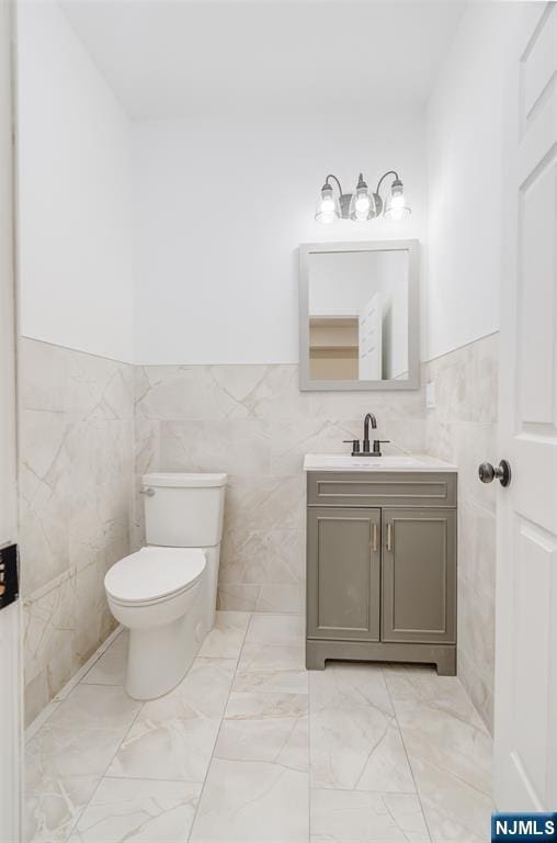 85 Myrtle Ave, Jersey City, NJ 07305 - half bathroom featuring tile walls, toilet, marble look tiles, vanity, and a wainscoted wall
