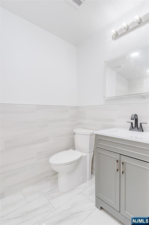 85 Myrtle Ave, Jersey City, NJ 07305 - bathroom with tile walls, toilet, vanity, marble look tile flooring, and wainscoting