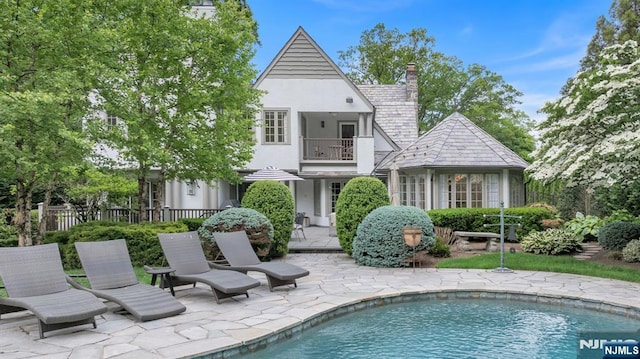 76 Wildwood Rd, Ridgewood, NJ 07450 - back of property with a balcony, stucco siding, an outdoor pool, a patio area, and a chimney
