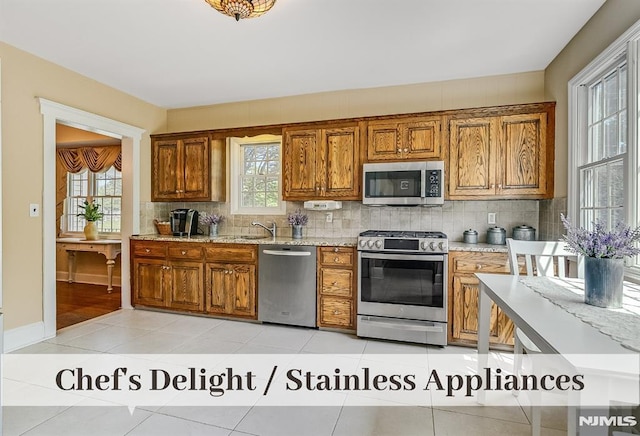 640 E Glen Ave, Ridgewood, NJ 07450 - kitchen featuring stainless steel appliances, brown cabinetry, backsplash, light stone counters, and light tile patterned floors