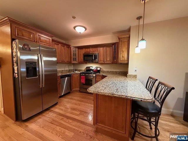124 68th St Unit 204, Guttenberg, NJ 07093 - kitchen with appliances with stainless steel finishes, a peninsula, brown cabinets, a kitchen breakfast bar, and glass insert cabinets