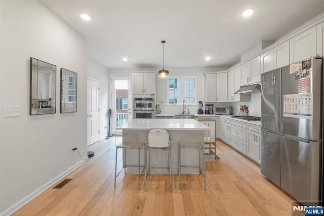 83 Landmark Ln, Fair Lawn, NJ 07410 - kitchen featuring appliances with stainless steel finishes, light countertops, a center island, light wood finished floors, and under cabinet range hood