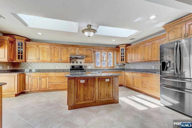 238 E Johnson Ave, Bergenfield, NJ 07621 - kitchen featuring stainless steel appliances, a skylight, under cabinet range hood, dark stone counters, and glass insert cabinets