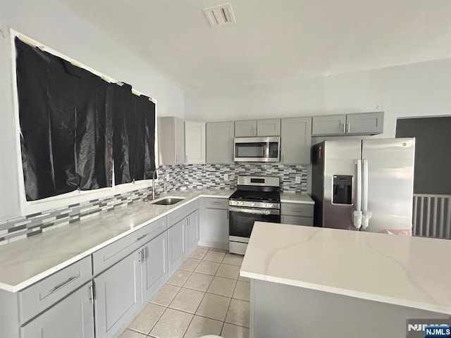 207 Tremont Ave, East Orange, NJ 07018 - kitchen featuring stainless steel appliances, gray cabinets, a sink, decorative backsplash, and light tile patterned floors