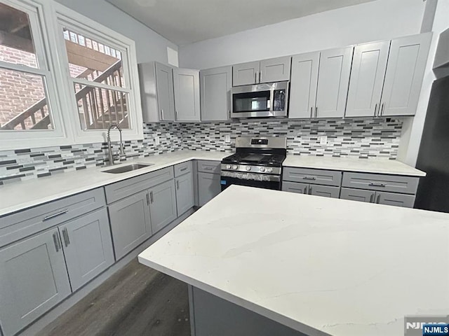 207 Tremont Ave, East Orange, NJ 07018 - kitchen featuring appliances with stainless steel finishes, gray cabinetry, a sink, dark wood-type flooring, and decorative backsplash