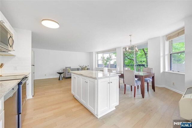 100 Grand Cove Way Unit 2D, Edgewater, NJ 07020 - kitchen featuring stainless steel appliances, light wood-style floors, white cabinets, a chandelier, and light stone counters
