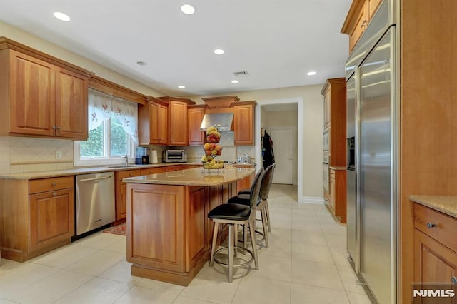 245 Forest Ave, Emerson, NJ 07630 - kitchen featuring appliances with stainless steel finishes, a kitchen island, tasteful backsplash, a kitchen bar, and brown cabinets