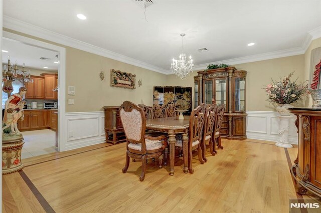 245 Forest Ave, Emerson, NJ 07630 - dining area with a chandelier, a decorative wall, wainscoting, light wood finished floors, and crown molding