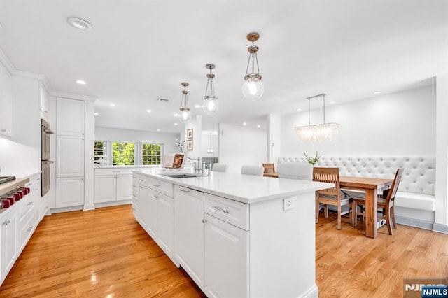 337 Vreeland Ave, Leonia, NJ 07605 - kitchen with a sink, light countertops, white cabinetry, a kitchen island with sink, and light wood-style flooring