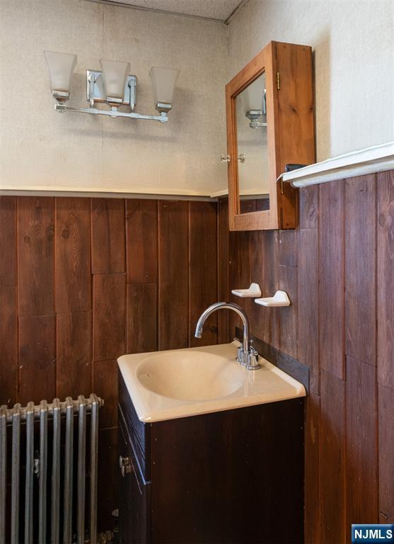50 Richards Ave, Dover Town, NJ 07801 - bathroom featuring radiator heating unit, vanity, wood walls, and a wainscoted wall