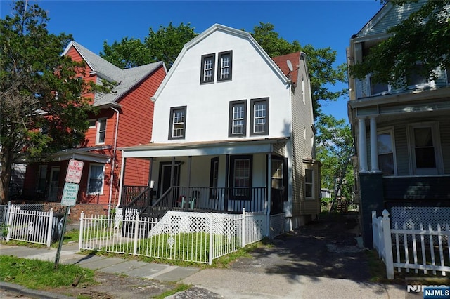116 19th St, East Orange, NJ 07017 - colonial inspired home featuring a porch, a fenced front yard, a gambrel roof, and stucco siding