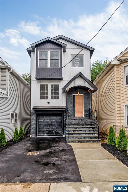 15 Monroe St, Garfield, NJ 07026 - view of front facade featuring stone siding, a garage, board and batten siding, and asphalt driveway