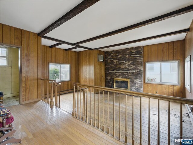 685 Maple Ave, Ridgefield, NJ 07657 - unfurnished living room featuring light wood-style floors, plenty of natural light, beam ceiling, wood walls, and a brick fireplace