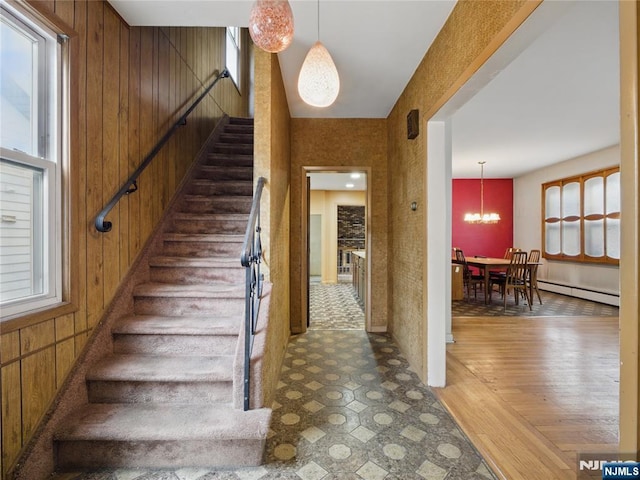 685 Maple Ave, Ridgefield, NJ 07657 - staircase with a baseboard radiator, wooden walls, healthy amount of natural light, a chandelier, and wood finished floors