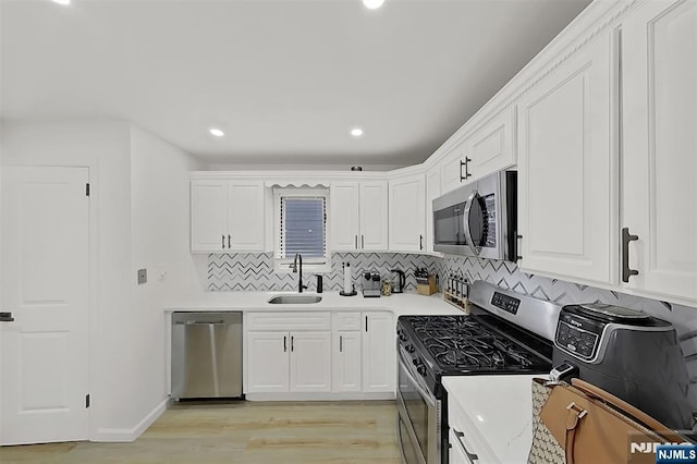107 Elm St, West Orange, NJ 07052 - kitchen featuring appliances with stainless steel finishes, a sink, white cabinetry, light wood finished floors, and backsplash
