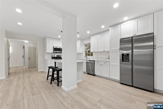428 Elm Ave, River Edge, NJ 07661 - kitchen featuring appliances with stainless steel finishes, light countertops, light wood-style floors, white cabinetry, and a kitchen bar