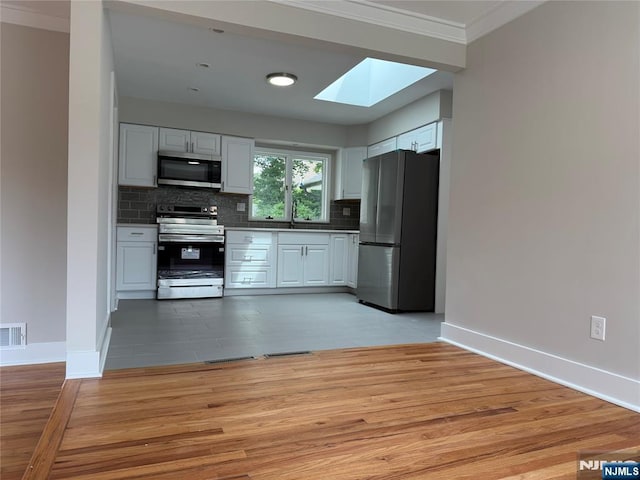 41 Woods Ave, Bergenfield, NJ 07621 - kitchen featuring appliances with stainless steel finishes, a skylight, crown molding, light wood-style floors, and white cabinetry