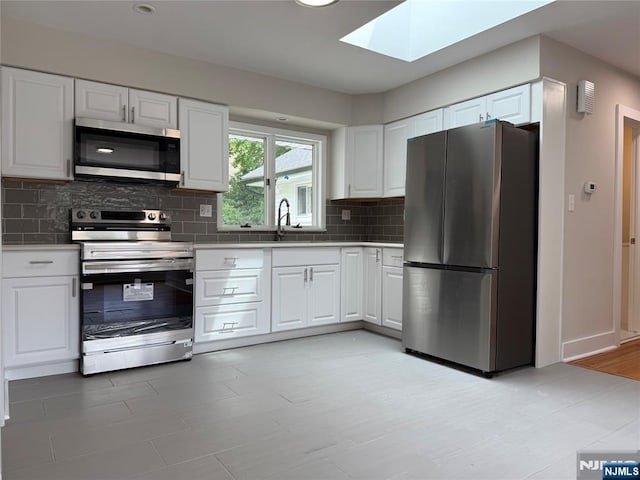 41 Woods Ave, Bergenfield, NJ 07621 - kitchen featuring appliances with stainless steel finishes, a skylight, tasteful backsplash, and white cabinets