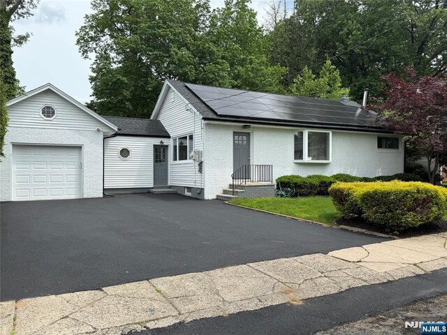 41 Woods Ave, Bergenfield, NJ 07621 - single story home with a garage, brick siding, roof mounted solar panels, a shingled roof, and driveway