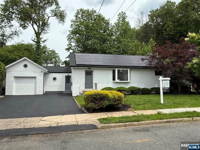 41 Woods Ave, Bergenfield, NJ 07621 - view of front facade featuring solar panels, brick siding, an attached garage, a front lawn, and driveway