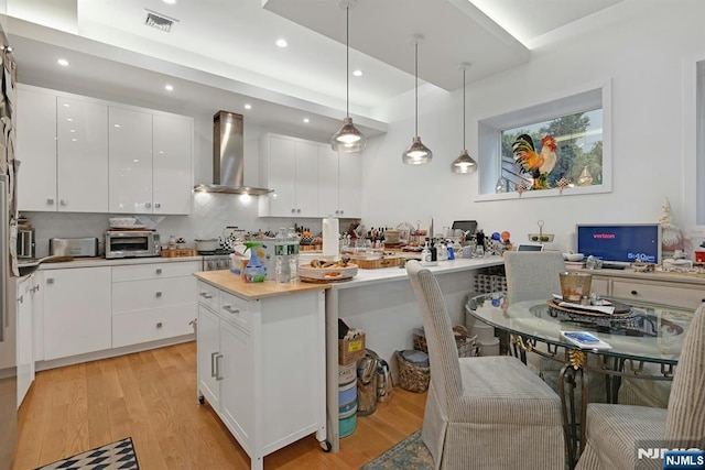 716 Undercliff Ave, Edgewater, NJ 07020 - kitchen with wall chimney range hood, light wood finished floors, white cabinetry, recessed lighting, and decorative backsplash