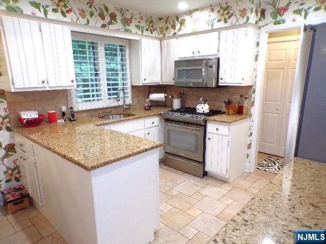 20 Carriage Ln, Ridgewood, NJ 07450 - kitchen with appliances with stainless steel finishes, a sink, white cabinetry, and backsplash