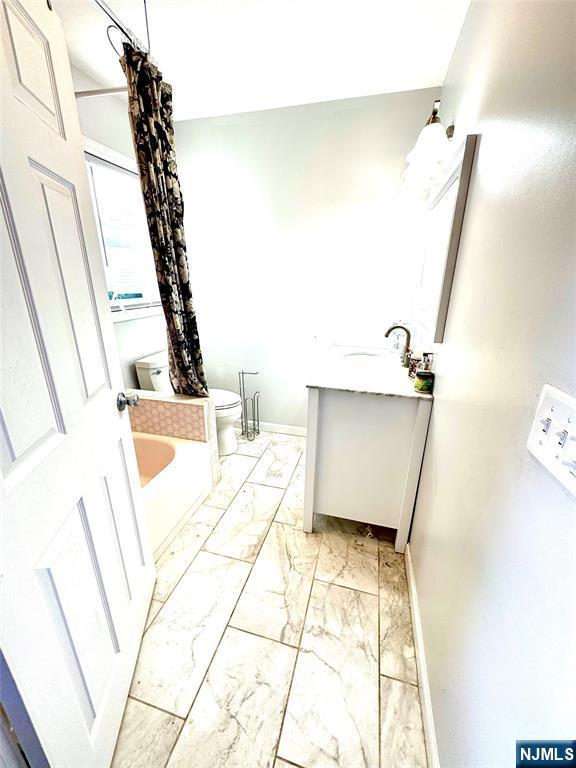 194 Elm Ave, Teaneck, NJ 07666 - bathroom featuring toilet, vanity, marble look tiles, baseboards, and a bathtub