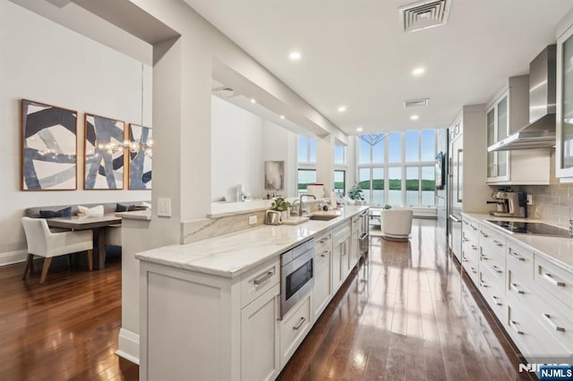 1360 Hamburg Tpke Unit 702, Wayne, NJ 07470 - kitchen featuring stainless steel microwave, black electric cooktop, wall chimney range hood, backsplash, and dark wood-style flooring