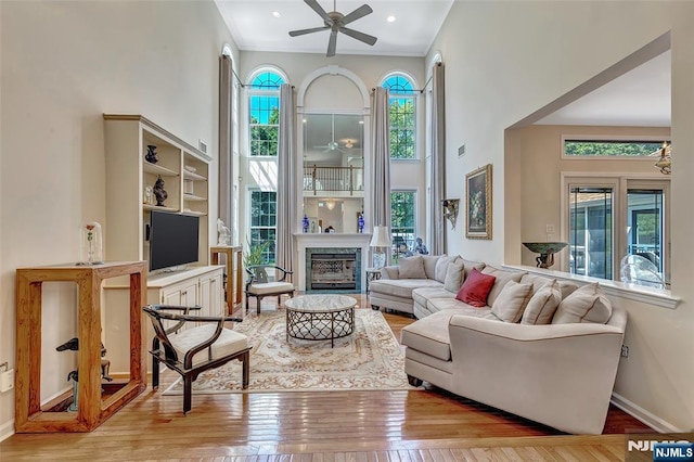  - living area with ceiling fan, hardwood / wood-style floors, a high ceiling, a glass covered fireplace, and baseboards