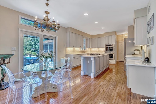  - kitchen with stainless steel appliances, light countertops, a chandelier, light wood-style floors, and tasteful backsplash