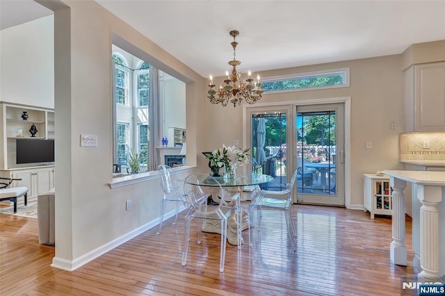  - dining room with light wood-style flooring, a fireplace, a chandelier, and baseboards