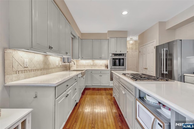  - kitchen with appliances with stainless steel finishes, light countertops, light wood finished floors, decorative backsplash, and white cabinetry