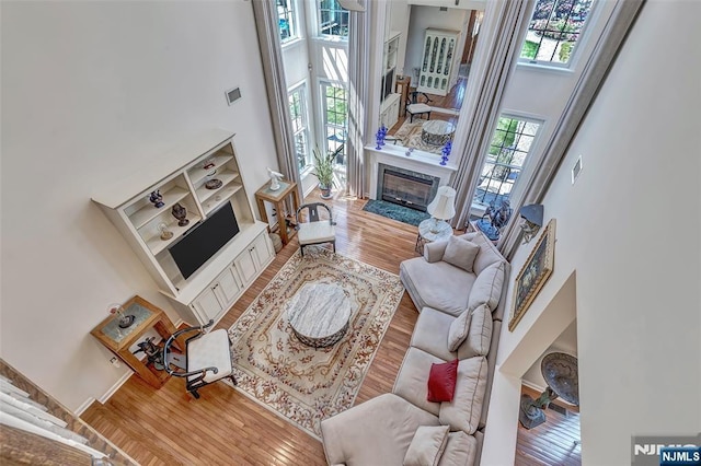  - living area with a towering ceiling, wood finished floors, and a fireplace with flush hearth