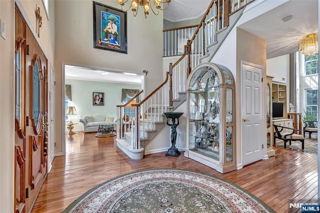  - entrance foyer with a chandelier, wood-type flooring, stairway, a towering ceiling, and baseboards