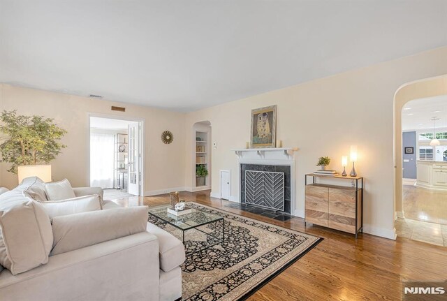 173 Sheridan Ave, Ho-Ho-Kus, NJ 07423 - living area featuring arched walkways, wood finished floors, a fireplace with flush hearth, and baseboards