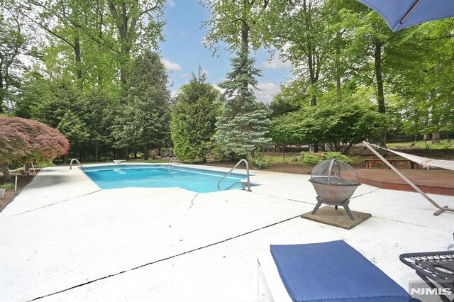 380 Hillside Ave, Allendale, NJ 07401 - outdoor pool with a patio, view of wooded area, and an outdoor fire pit