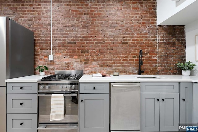 606 1st St Unit 1, Hoboken, NJ 07030 - kitchen with appliances with stainless steel finishes, brick wall, a sink, gray cabinetry, and light countertops