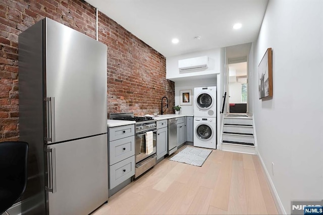 606 1st St Unit 1, Hoboken, NJ 07030 - kitchen with appliances with stainless steel finishes, stacked washer and clothes dryer, a wall mounted air conditioner, gray cabinetry, and light countertops