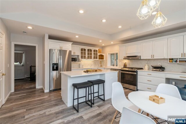 62 Valley Rd, Glen Rock, NJ 07452 - kitchen with appliances with stainless steel finishes, wood finished floors, a kitchen island, a kitchen breakfast bar, and white cabinets