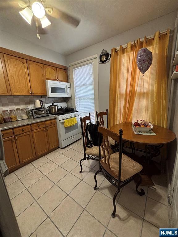 65 Dey St, Paterson, NJ 07503 - kitchen with white appliances, brown cabinetry, light tile patterned flooring, tasteful backsplash, and a ceiling fan