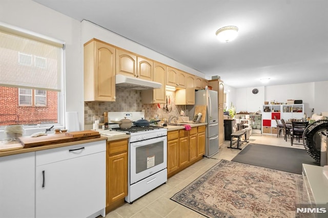 755 Jefferson Ave, Cliffside Park, NJ 07010 - kitchen featuring white gas stove, under cabinet range hood, backsplash, light tile patterned floors, and freestanding refrigerator