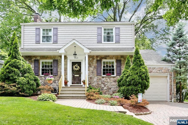 145 Concord Dr, River Edge, NJ 07661 - view of front of house with stone siding, a chimney, a front yard, decorative driveway, and a garage