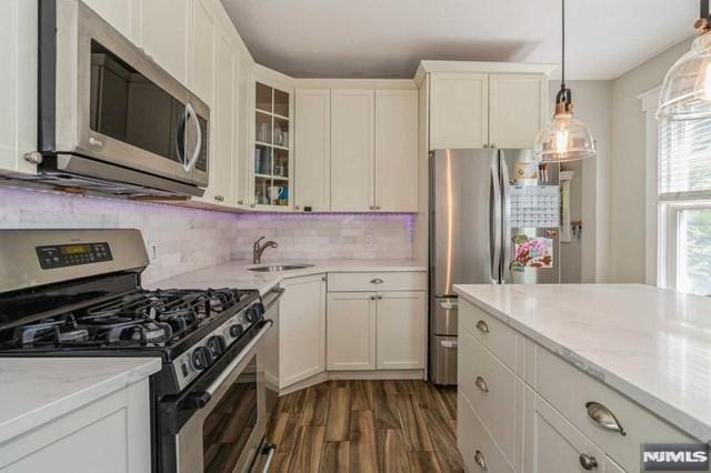 129 Phelps Ave, Englewood, NJ 07631 - kitchen featuring appliances with stainless steel finishes, a sink, dark wood-style floors, decorative backsplash, and glass insert cabinets