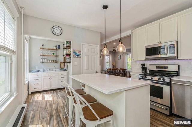 129 Phelps Ave, Englewood, NJ 07631 - kitchen with appliances with stainless steel finishes, wood finished floors, a kitchen breakfast bar, white cabinets, and decorative backsplash