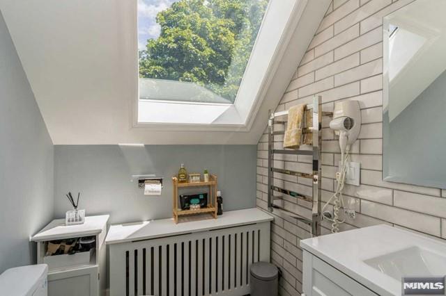 129 Phelps Ave, Englewood, NJ 07631 - half bath with radiator, toilet, decorative backsplash, vaulted ceiling, and vanity