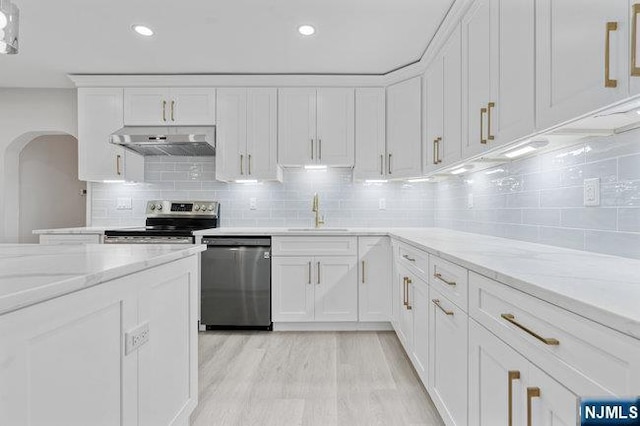 310 Spring Valley Rd, Paramus, NJ 07652 - kitchen featuring appliances with stainless steel finishes, range hood, a sink, arched walkways, and white cabinetry