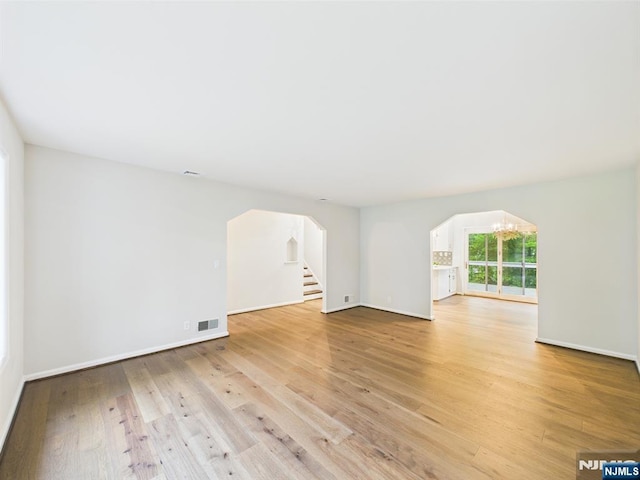 995 Andover Ter, Ridgewood, NJ 07450 - unfurnished living room with arched walkways, a chandelier, light wood-style flooring, and baseboards